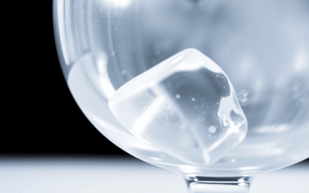 Közeli kép egy tiszta, kristályszerű jégkockáról egy átlátszó koktélpohárban, lágy világítással és sötét, elmosódott háttérrel.