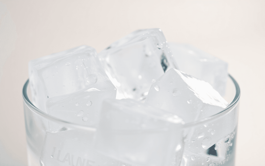 Közeli kép tiszta jégkockákról, amelyek olvadnak egy pohárban, lágy tükröződésekkel egy semleges háttér előtt, kiemelve a tisztaságot és frissességet.