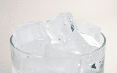 Közeli kép tiszta jégkockákról, amelyek olvadnak egy pohárban, lágy tükröződésekkel egy semleges háttér előtt, kiemelve a tisztaságot és frissességet.