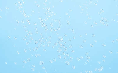 Közelkép apró, átlátszó mikroműanyag részecskékről, amelyek tiszta vízben lebegnek egy lágy kék háttér előtt, kiemelve a víz tisztaságát és a szenn...