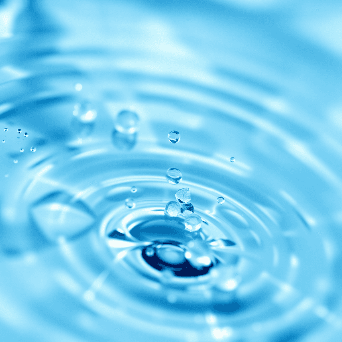 Közelkép tiszta vízcseppekről és hullámokról, finom ragyogó részecskékkel, orvosi hangulatú kék-fehér háttér előtt, a tisztaság és egészség jelképeként.
