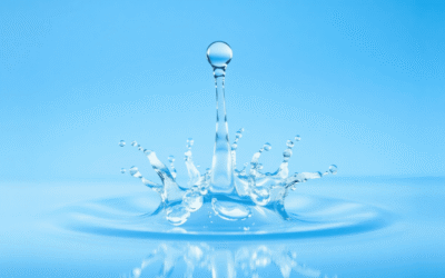 Tiszta, kristálytiszta vízcsepp, amely szimmetrikus klaszterekre törik, lágy kék háttérrel és fénylő energiahullámokkal, a tisztított víz és az éle...